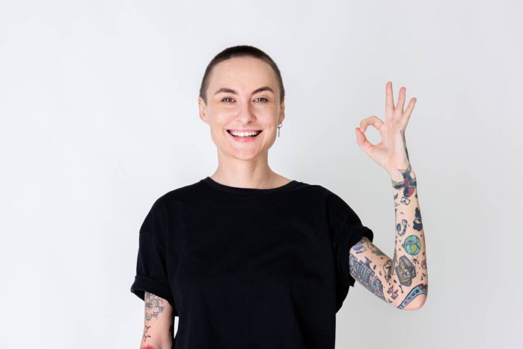Skinhead model with tattoos in black T shirt with an okay hand sign