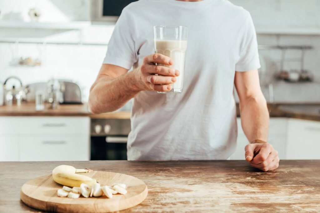 cropped shot of athletic man holding glass with banana protein shake at home