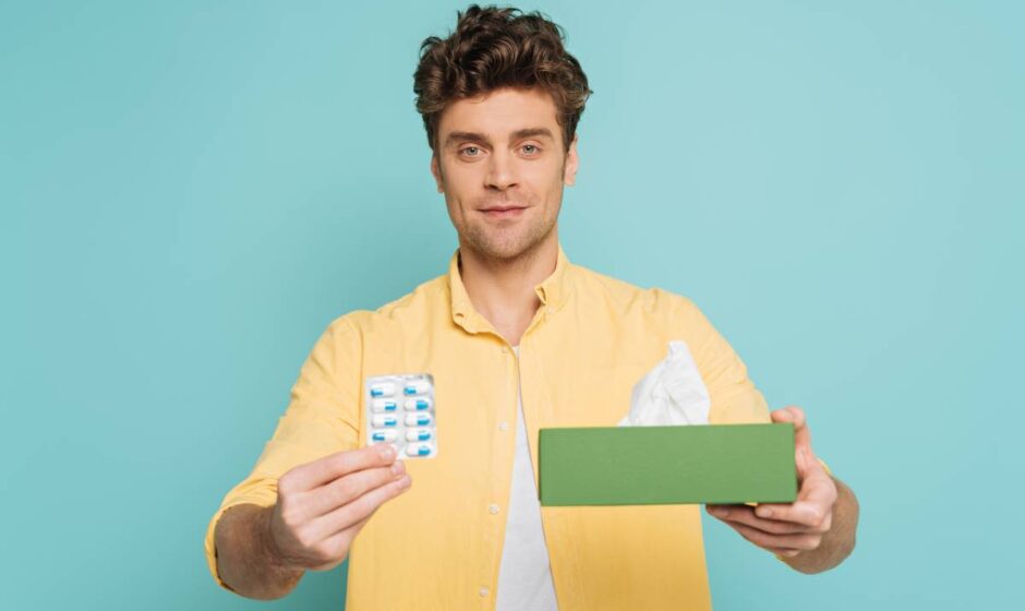 Front view of man showing blister pack with pills and box with napkins and looking at camera